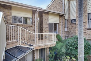 A residential building with a balcony, a garage, and a brick facade. - Batehaven Coastal Escape | Pool & Bay Views (BATEHAVEN)