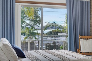 A room with a bed, a chair, and a view of a residential area through a large window.