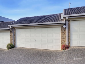 A residential garage with a tiled roof, brick walls, and a gravel driveway. - Batehaven Coastal Escape | Pool & Bay Views (BATEHAVEN)