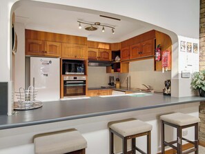 A modern kitchen with wooden cabinets, stainless steel appliances, and a bar area with stools.