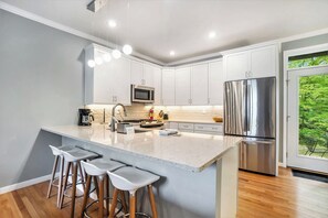 A modern kitchen with white cabinets, a stainless steel refrigerator, a microwave, and a large island with bar stools. - 🏖️Sleepy Hollow Beach Resort, Terrace 20 – Family Fun on Lake Michigan! (South Haven)