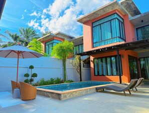 Ein modernes Haus mit Swimmingpool, Sitzgelegenheit im Freien und einem großen Sonnenschirm.