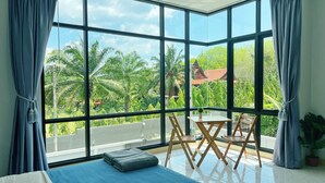 A room with large windows, a bed, a small table with chairs, and a potted plant. - Aonang Nine Poolvilla (Krabi)