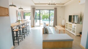 A modern living room with a sofa, dining area, and TV. - Aonang Nine Poolvilla (Krabi)