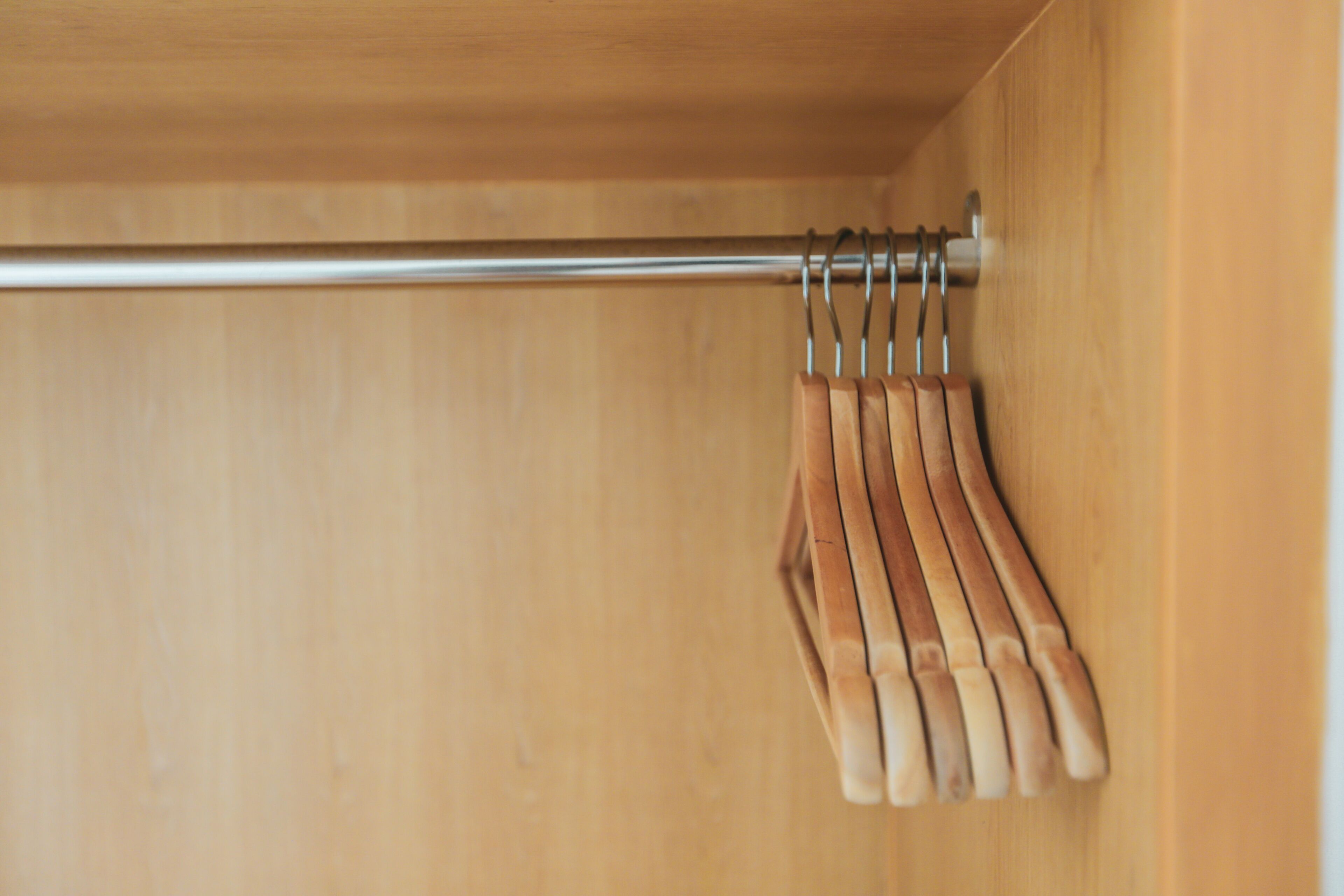A wooden closet with a metal rod and wooden hangers.