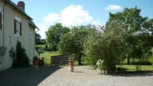 Une allée de gravier mène à une maison dotée d’un mur en pierre et agrémentée de plantes en pot.