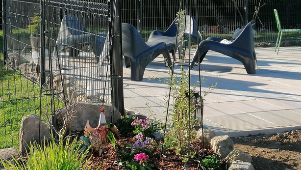 Un espace extérieur clos, comprenant un parterre de fleurs, un oiseau et une sculpture.