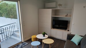 Un salón moderno con un sofá gris, dos mesas redondas, un televisor de pantalla plana y un ventanal corredero que da a un balcón.