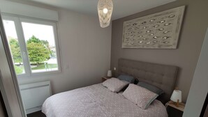 Un dormitorio con cama, ventana, radiador, un cuadro de peces y una lámpara colgante.