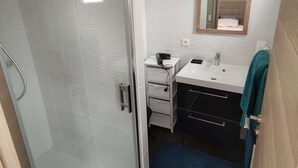 Un baño moderno con mampara de vidrio, un lavabo blanco con espejo y una toalla azul en el suelo.