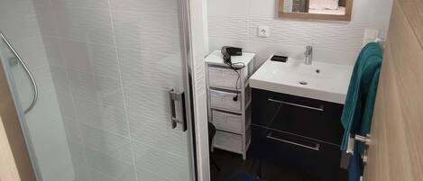 A modern bathroom with a glass shower door, a white sink with a mirror above, and a blue towel on the floor.
