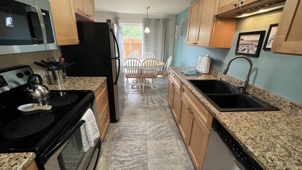 A kitchen with granite countertops, wooden cabinets, a black refrigerator, a stove, and a sink. - Riverwalk Condominiums #11 – Ground Floor with Private Patio, Close to Beach and (Seaside)