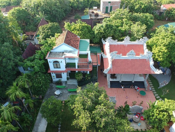 An aerial view of a traditional building with a red roof and white walls, surrounded by lush greenery.