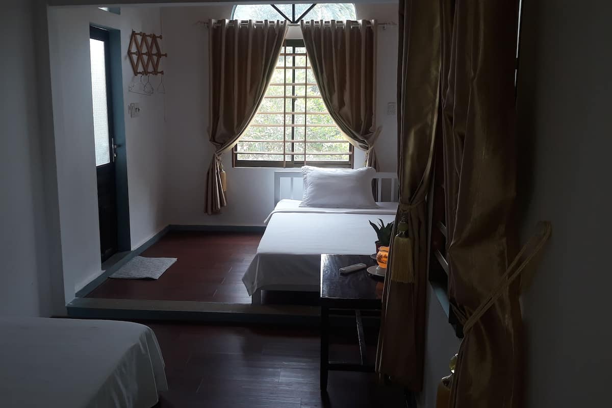 A hotel room with a bed, a small table, a window with curtains, and a door.