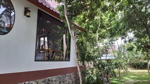 A house with a stone foundation, a red and white exterior, and a window overlooking a garden with a stone pathway. - Tropical Valley Homestay (Phong Nha)