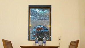 A small room with a wooden table and two wooden chairs, a window with a view of trees, and a wall socket. - Tropical Valley Homestay (Phong Nha)