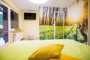 A bedroom with a bed, a TV mounted on the wall, a window, and a door.
