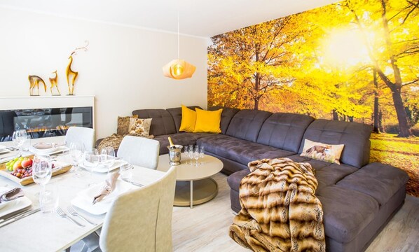A modern living room with a grey sofa, yellow cushions, a fireplace, and a dining area set for a meal.