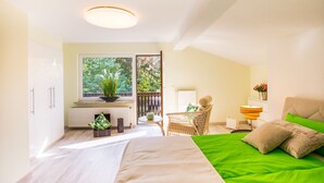 A bright room with a bed, a chair, a table, and a window with a view of greenery. - Separate, comfortable house for 6-8 guests - 3 bedrooms, 3 bathrooms (Bad Sachsa)