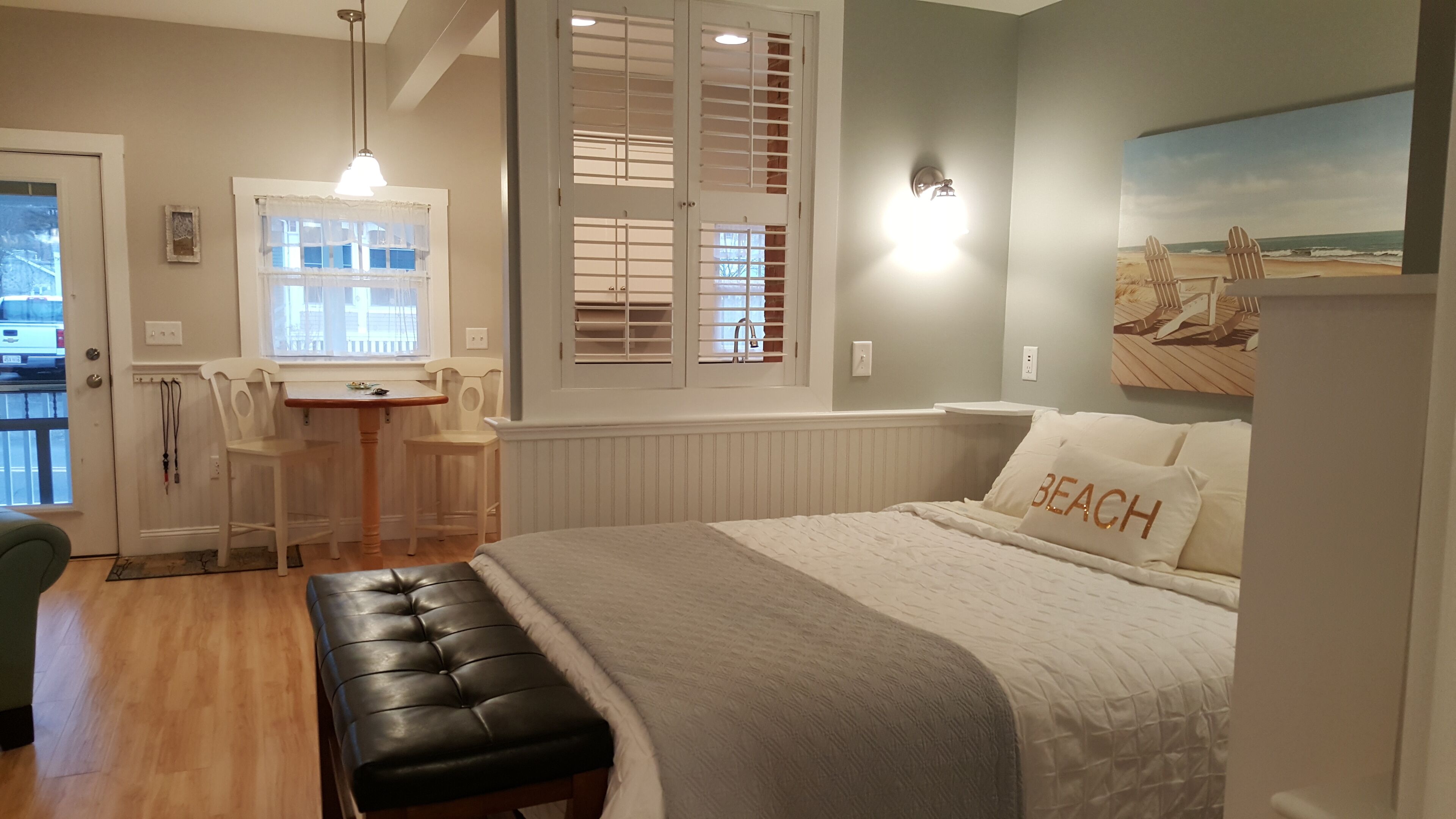 A bedroom with a bed, bench, desk, chairs, and a window with blinds.