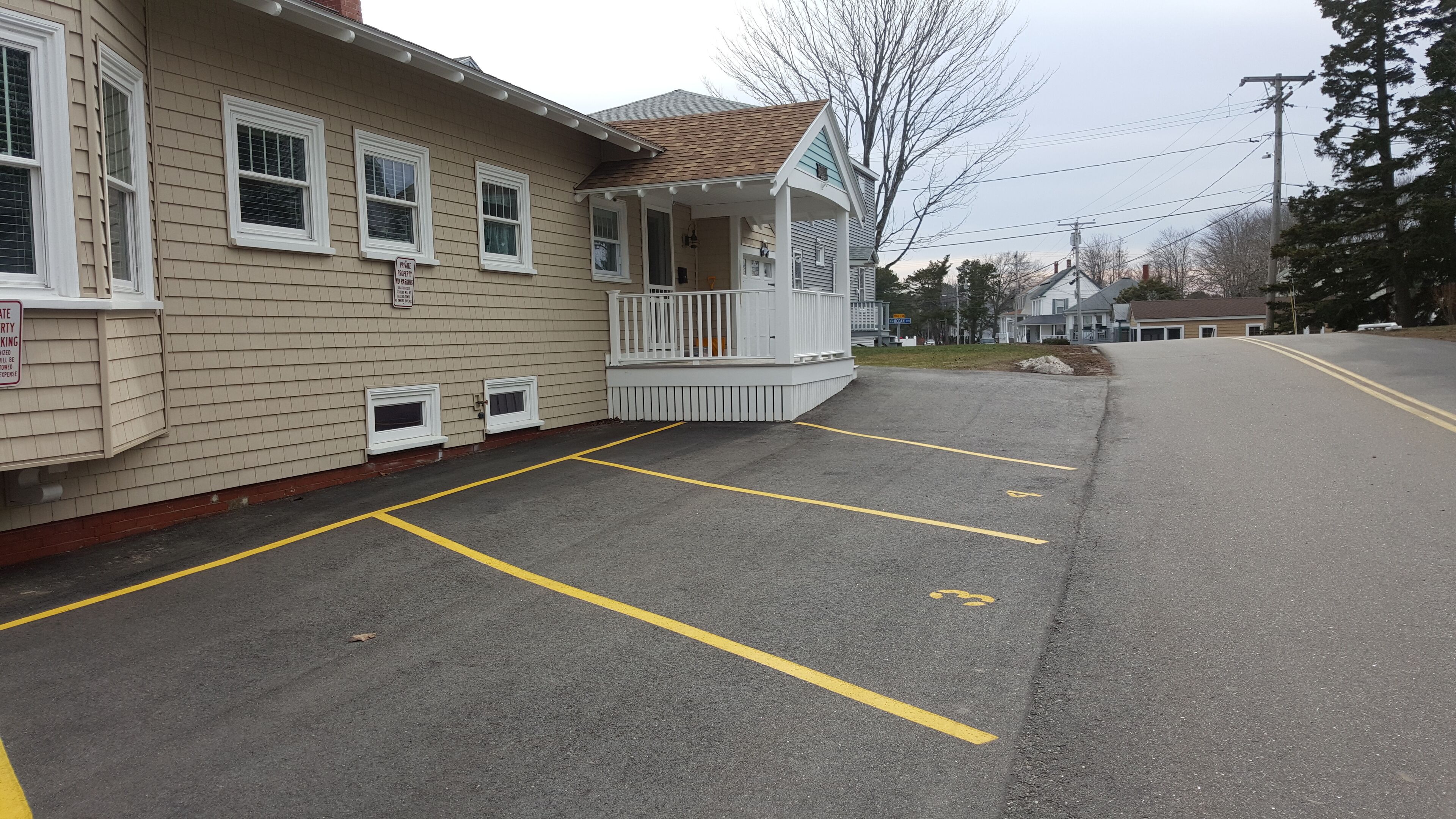 A residential building with a covered porch and a parking lot with marked spaces.