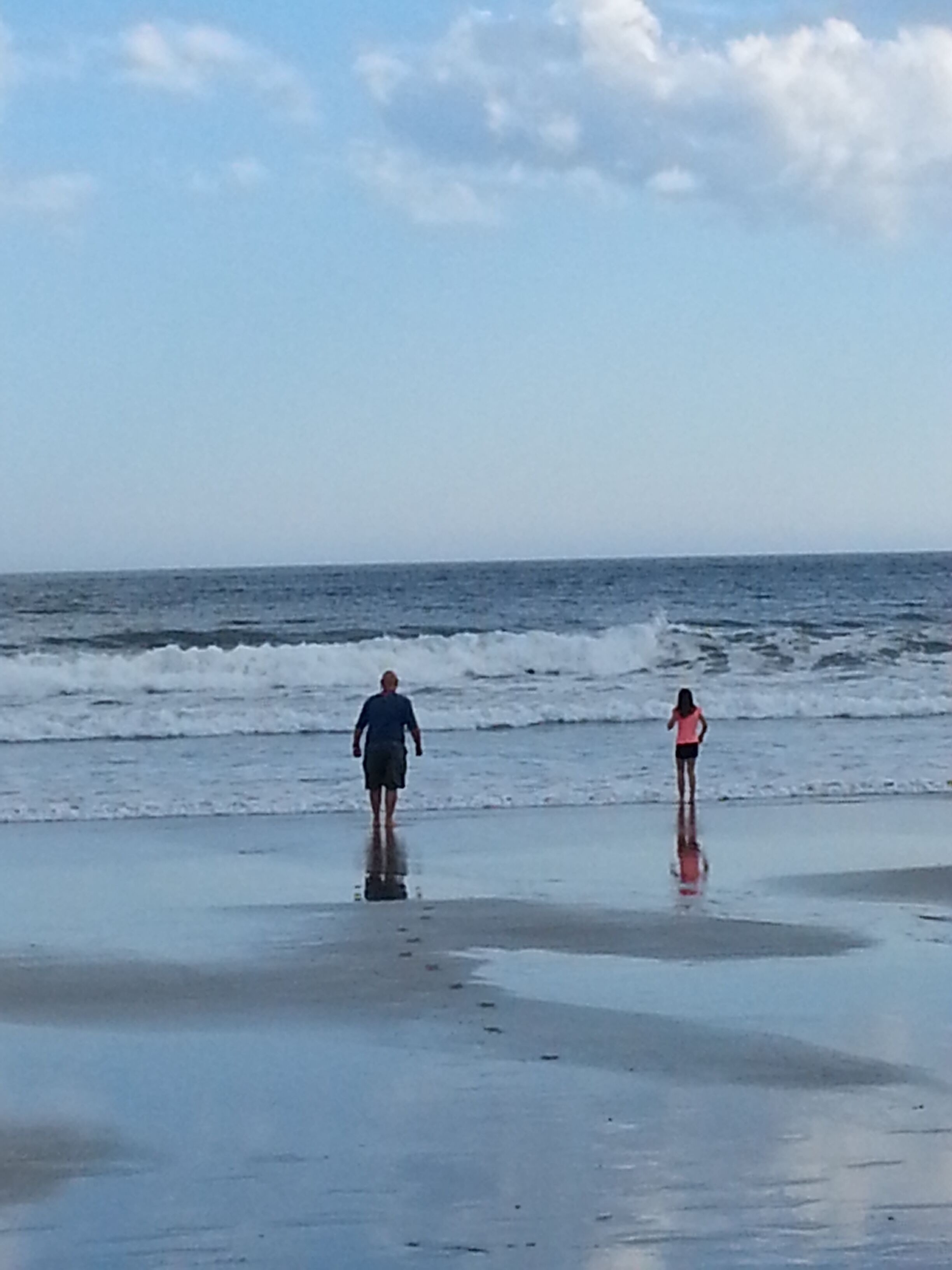 A beach with two people walking towards the water.