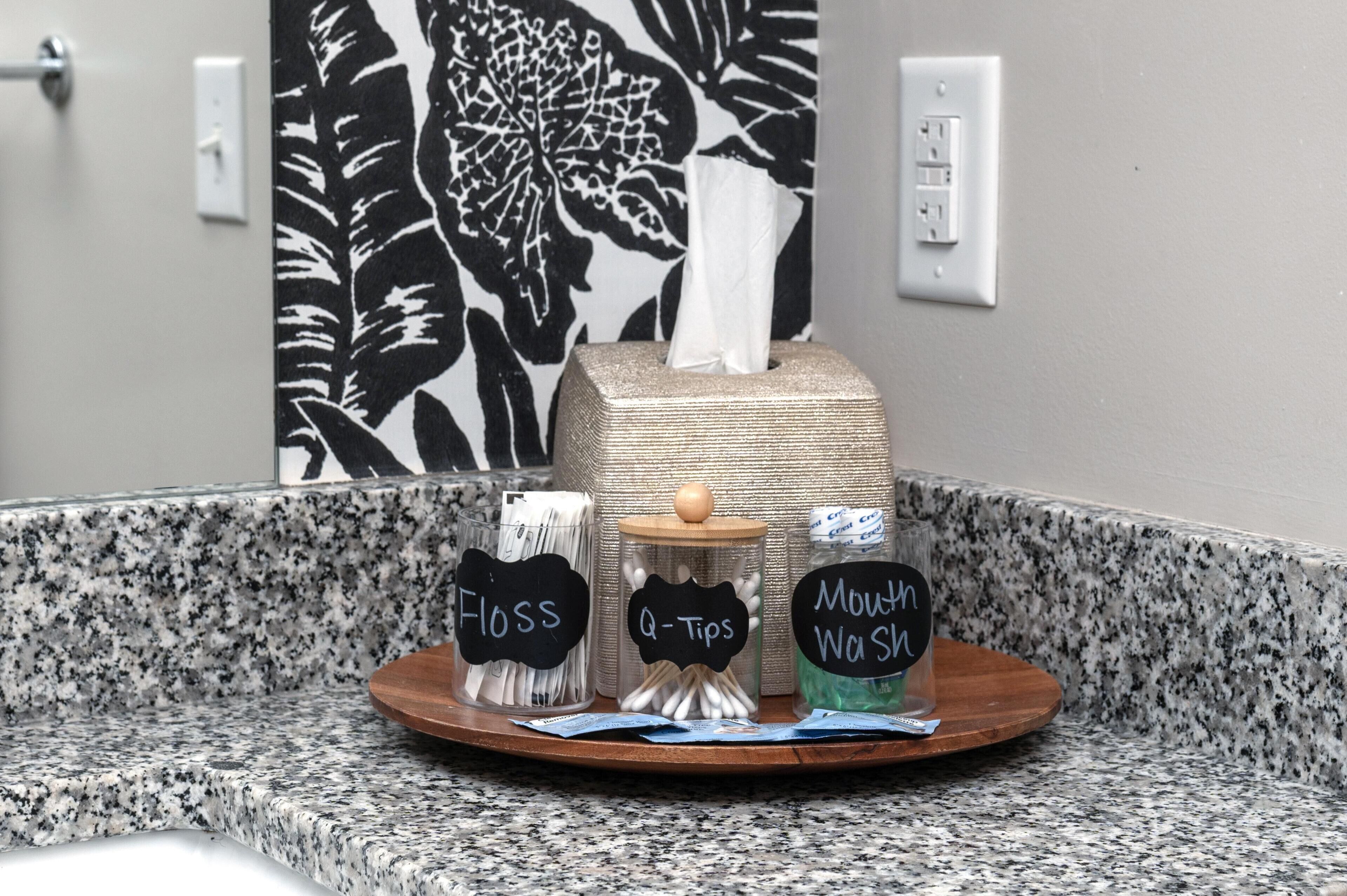 A bathroom counter with a tissue box, a container labeled 'Floss', a container labeled 'Q-Tips', and a container labeled 'Mouth Wash'.