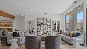 Un salon moderne avec un canapé gris, deux poufs gris, une table basse blanche et un meuble mural décoratif.