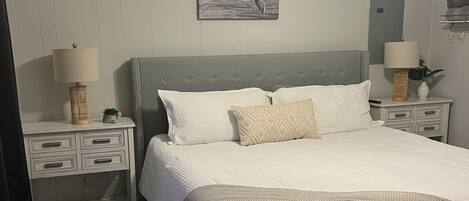 A bedroom with a bed, nightstands, a ceiling fan, a wall-mounted painting, and a door.