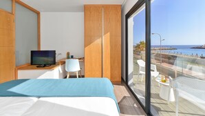 A modern hotel room with a bed, a desk with a TV, a balcony with chairs, and a view of the sea. - Morea Suites 1 by VillaGranCanaria (Mogan)