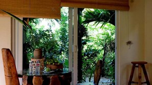 A room with a glass door leading to a garden, a round table with chairs, and a small stool. - Mercy Homestay - Experience Vietnam rural life (Individual) (Hội An)