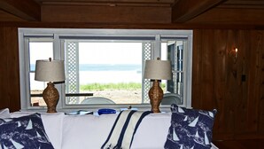 A bedroom with a large window, a bed with white bedding, two lamps, and a view of the beach. - Luxury Oceanfront 5 Bedroom 3.5 Bathroom Private Parsons Beachfront Paradise (Kennebunk)