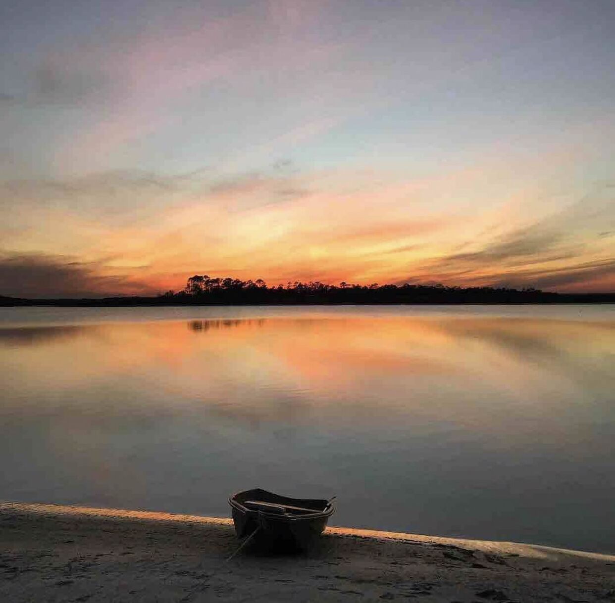 A calm lake at sunset with a boat on the shore.