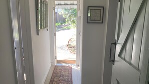 A hallway with a wooden floor, a patterned rug, a door with a handle, and a framed picture on the wall. - Colony Haven in the Oaks (Atascadero)