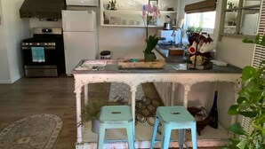 A kitchen with a central island, two stools, a refrigerator, an oven, and a window with blinds. - Colony Haven in the Oaks (Atascadero)