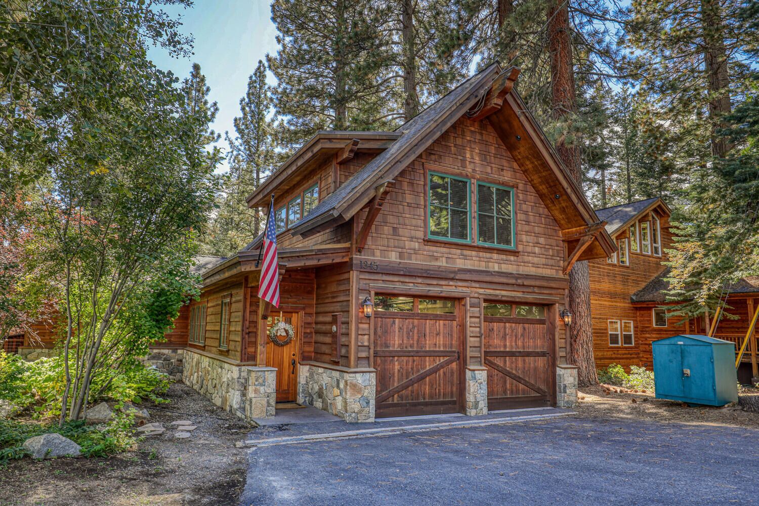 A rustic log cabin with a stone foundation, two garage doors, and an American flag.