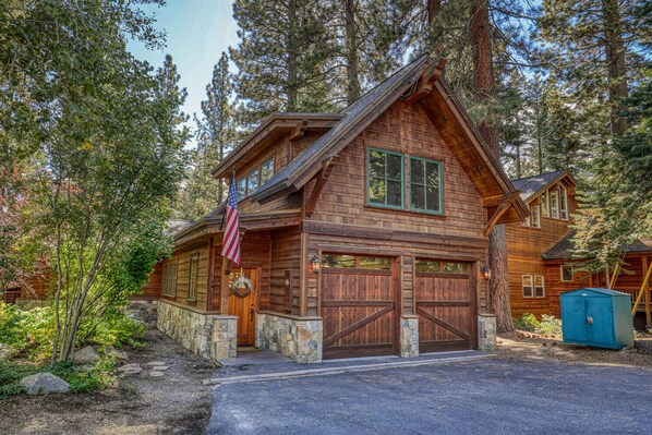 A rustic log cabin with a stone foundation, two garage doors, and an American flag.