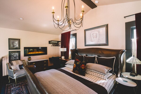 A spacious bedroom with a large bed, a chandelier, a television, and a framed artwork on the wall. - Private Lofted Downtown Studio (Sebastopol)