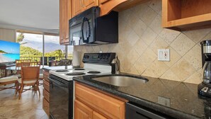 A kitchen with wooden cabinets, a black microwave, a stove, and a large window overlooking a scenic view.