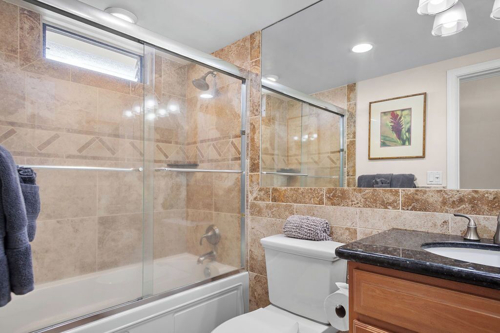 A modern bathroom with a glass-enclosed shower, a white toilet, and a sink with a marble countertop.