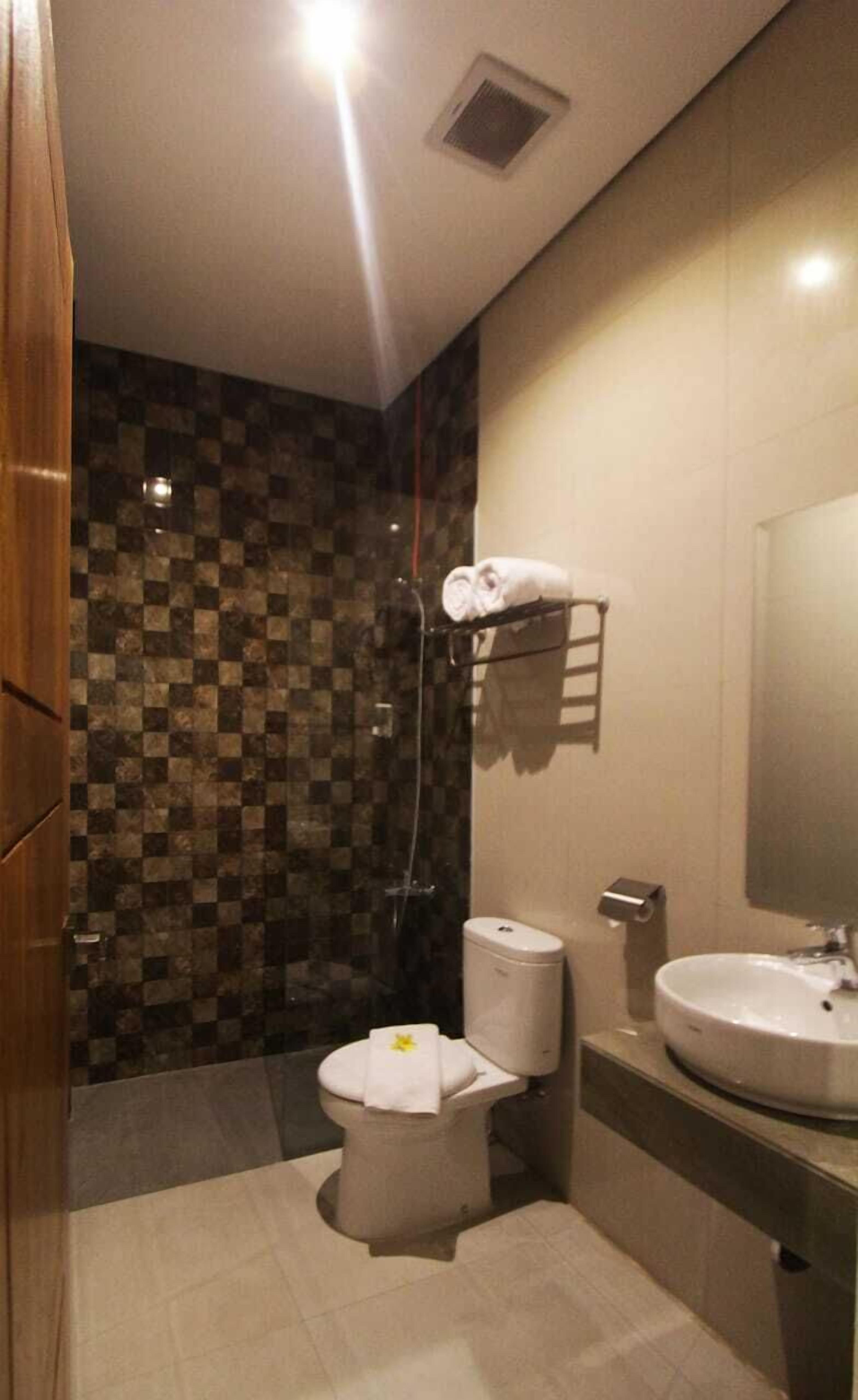 Un baño moderno con pared de baldosas a cuadros, un inodoro con toalla, un lavabo y una ducha.