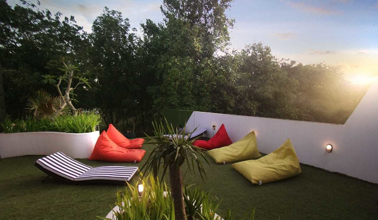 A rooftop garden with artificial grass, a lounge chair, and colorful cushions.