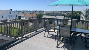 A wooden deck with a table and chairs, a turquoise umbrella, and a view of houses and water. - Location!! Ocean views. Easy walk to beaches, restaurants, shops. Quiet street.  (Middletown)