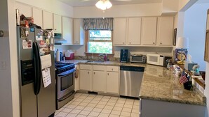 A kitchen with white cabinets, a stove, a dishwasher, a microwave, and a window with a view of greenery. - Location!! Ocean views. Easy walk to beaches, restaurants, shops. Quiet street.  (Middletown)