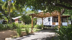 Un espace extérieur abrité, doté d’une pergola en bois, entouré d’une végétation luxuriante et bordé d’un chemin de gravier.