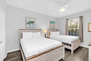 A bedroom with two beds, a ceiling fan, and artwork on the walls.