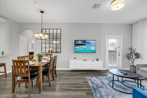 A modern living room with a dining area, a flat-screen TV mounted on the wall, a sofa, and a coffee table.