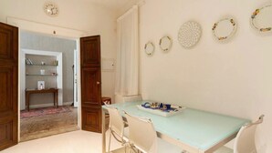 A dining area with a light blue table and white chairs, a small side table with a tray, and a bookshelf in the background. - Charming apartment not far from Piazza San Marco (Venezia)