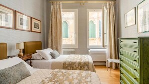 A hotel room with two beds, a dresser, and a window with a view of a building. - Charming apartment not far from Piazza San Marco (Venezia)