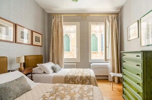 Hotellihuone, jossa on kaksi sänkyä, lipasto ja ikkuna, josta on näkymä rakennukseen.